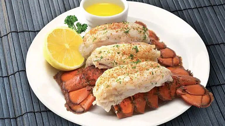 Plate of 3 well-seasoned cooked lobster tails with a bowl of butter and half cut lemon